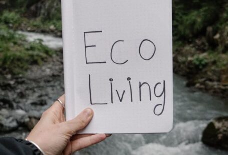 Sustainable Living - Person Holding a Notebook with a Text "Eco Living" on the Background of a River in a Forest